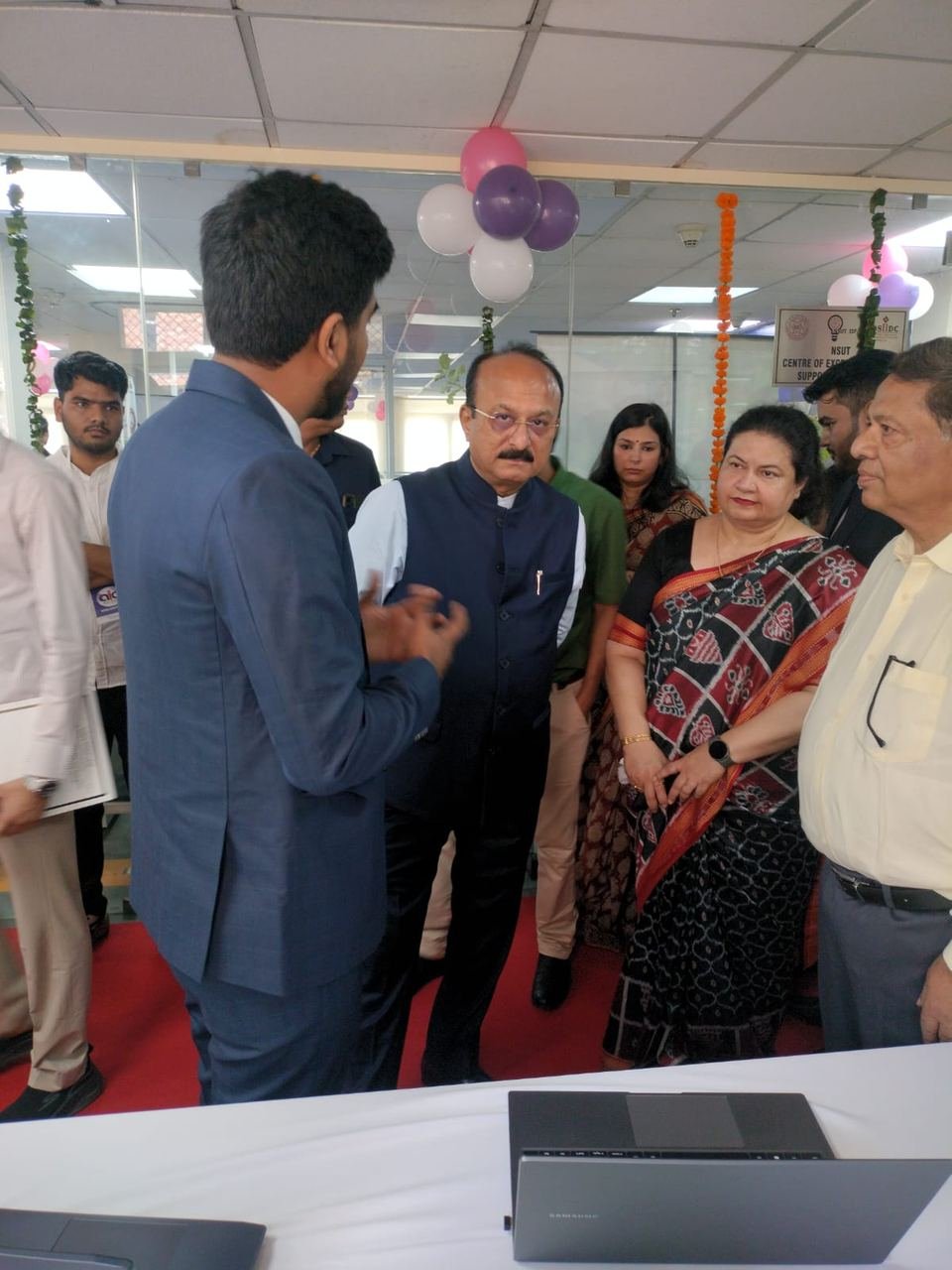 A Zoffer team member in a blue suit explaining the product to a group of guests from the inauguration at the kiosk, with laptops open on the table