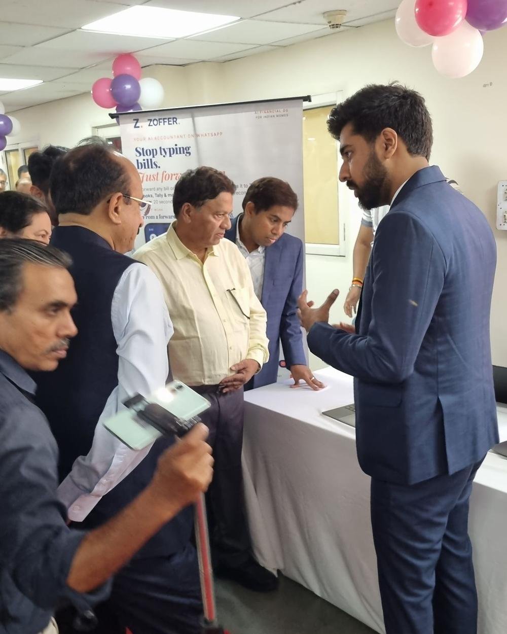 A Zoffer team member in a navy suit explaining the product to guests at the kiosk, with the Stop typing bills. Just forward them. standee behind the table