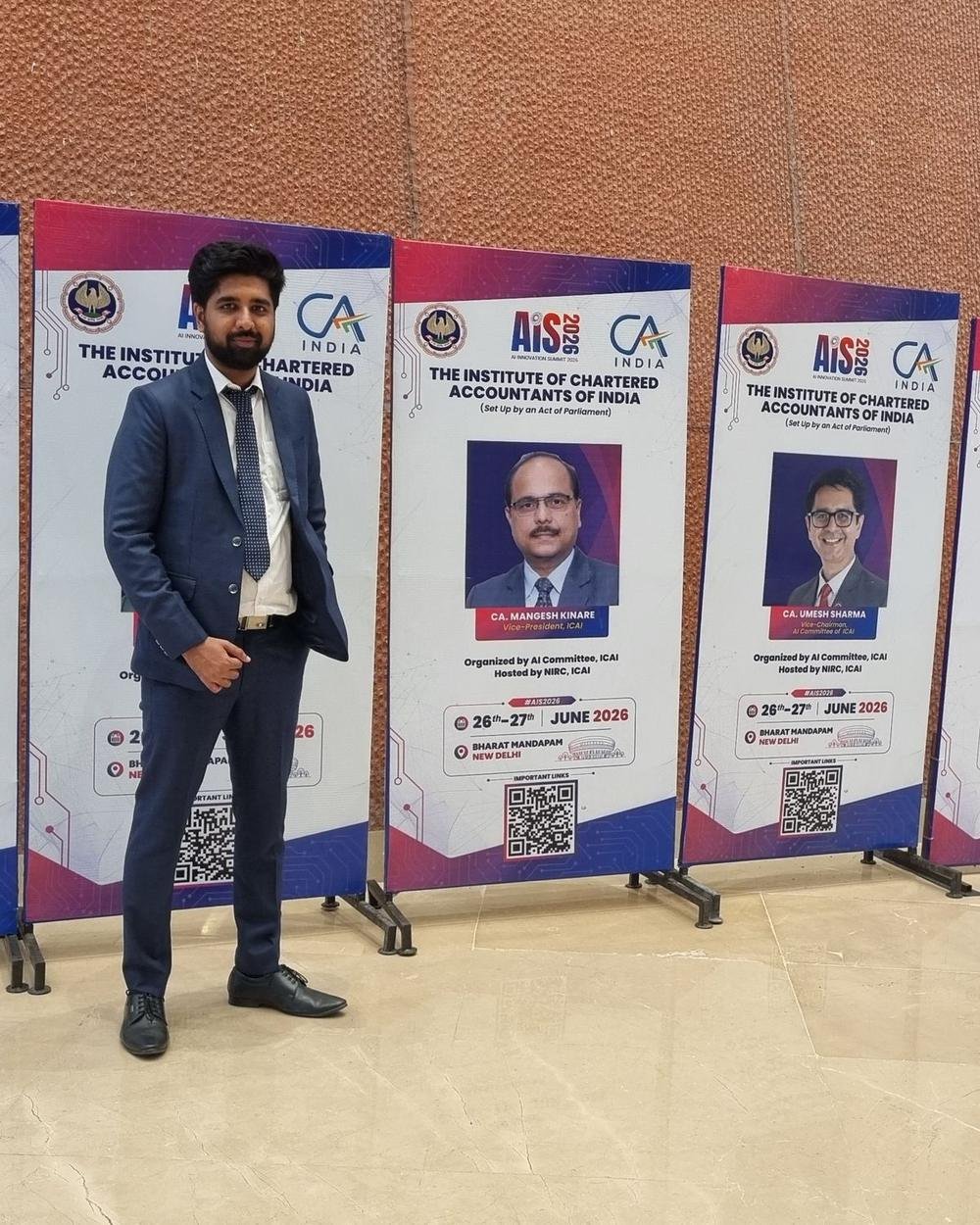 A Zoffer team member in a navy suit standing among a row of AIS 2026 standees from the Institute of Chartered Accountants of India at Bharat Mandapam