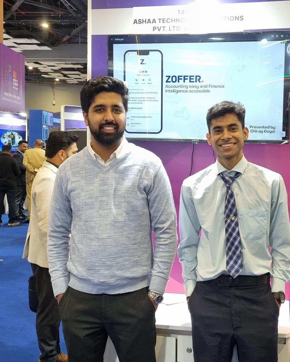 Two Zoffer team members standing in front of an expo stand screen showing Zoffer, with the tagline Accounting easy and Finance Intelligence accessible, on the busy India AI Impact Expo floor