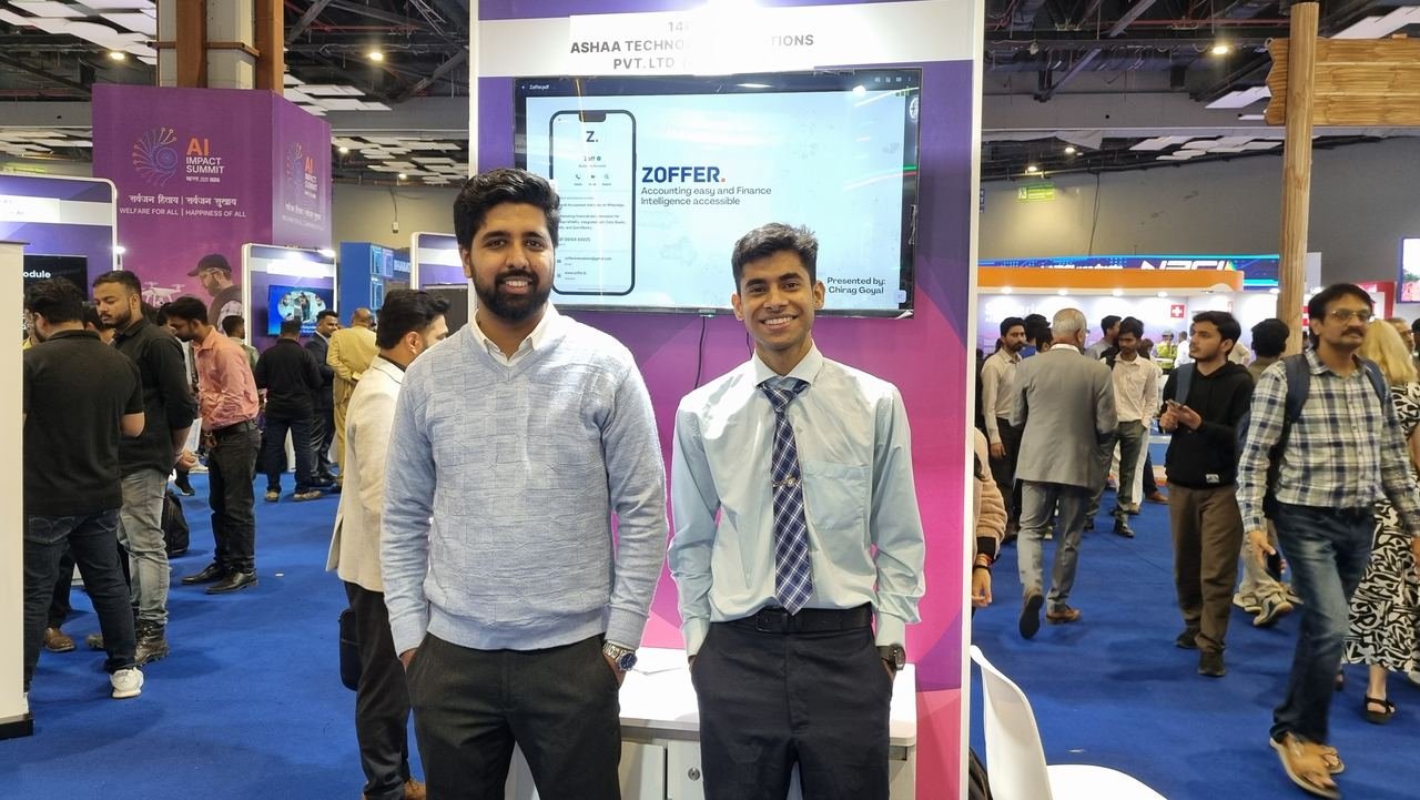 Two Zoffer team members standing in front of an expo stand screen showing Zoffer, with the tagline Accounting easy and Finance Intelligence accessible, on the busy India AI Impact Expo floor